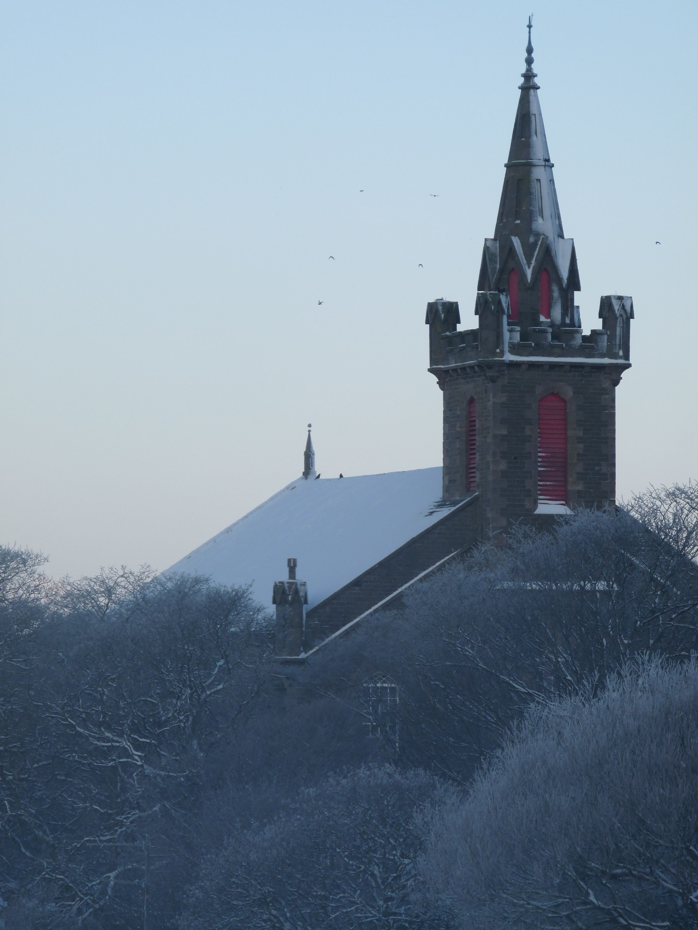 Una chiesa con un campanile a guglia e una porta rossa, circondata da alberi innevati.