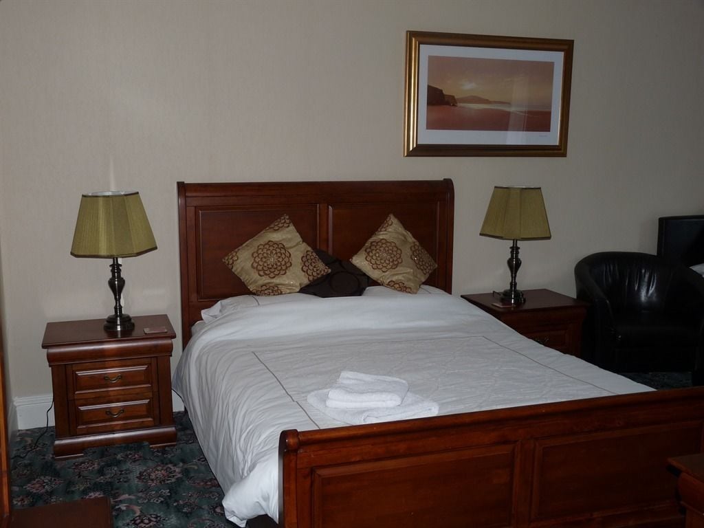 A neatly made bed with a wooden headboard, two bedside tables with lamps, a framed picture on the wall, and a black leather chair.