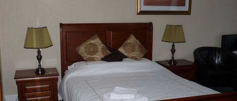 A neatly made bed with a wooden headboard, two bedside tables with lamps, a framed picture on the wall, and a black leather chair.