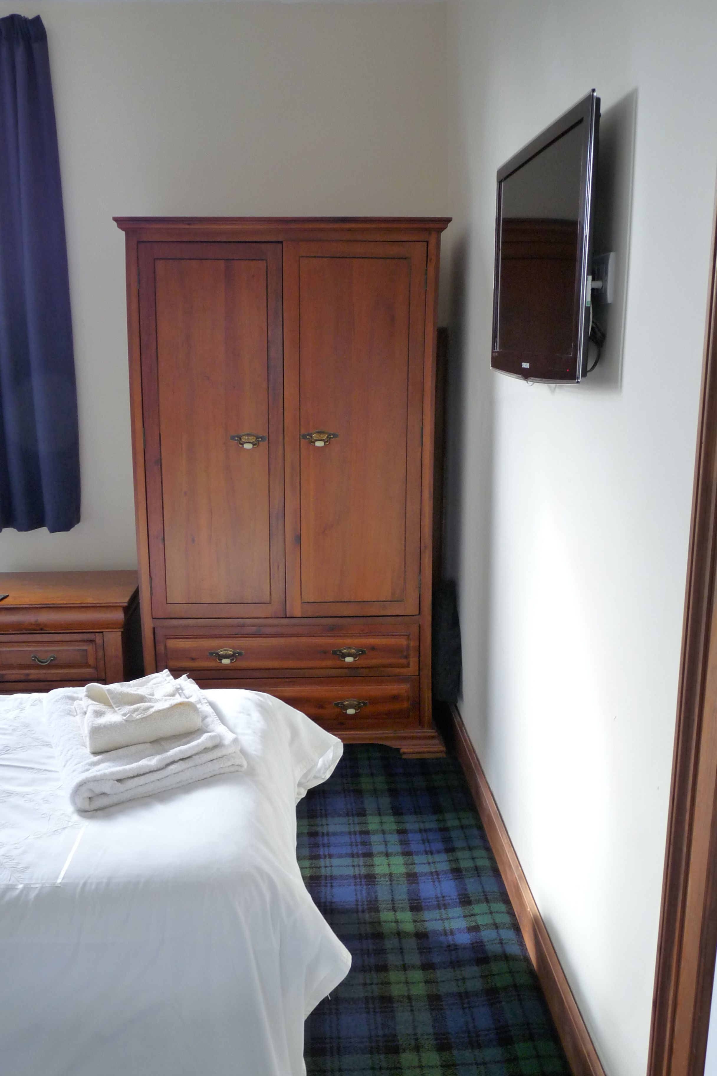 A bedroom with a bed, a wooden wardrobe, a television, and a plaid-patterned floor.
