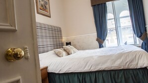 Une chambre d’hôtel avec un lit, une tête de lit, une table de chevet, une fenêtre avec des rideaux et une porte avec une poignée.