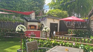 An outdoor patio area with a brick oven, wooden tables, and chairs. - The Inn at Kippen (Stirling)