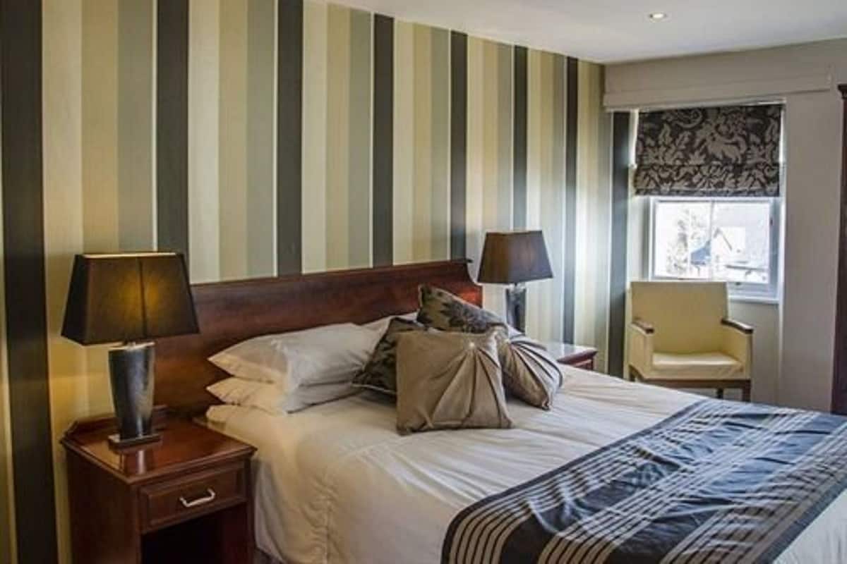 A hotel room with a striped wall, a bed with white linens, two bedside tables with lamps, and a window with a view.