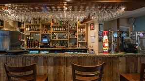 A bar area with wooden bar counter, multiple shelves of liquor bottles, and a variety of glassware. - The Inn at Kippen (Stirling)
