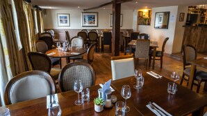 A restaurant with wooden tables and chairs, wine glasses, and a bar area. - The Inn at Kippen (Stirling)