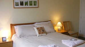 Una cama bien hecha con sábanas blancas, una lámpara de noche y un cuadro en la pared.