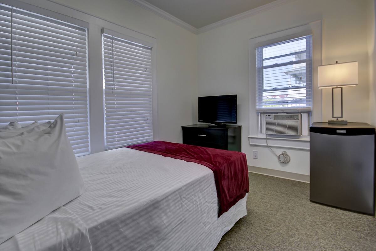 Un dormitorio con cama, televisor, escritorio y lámpara.