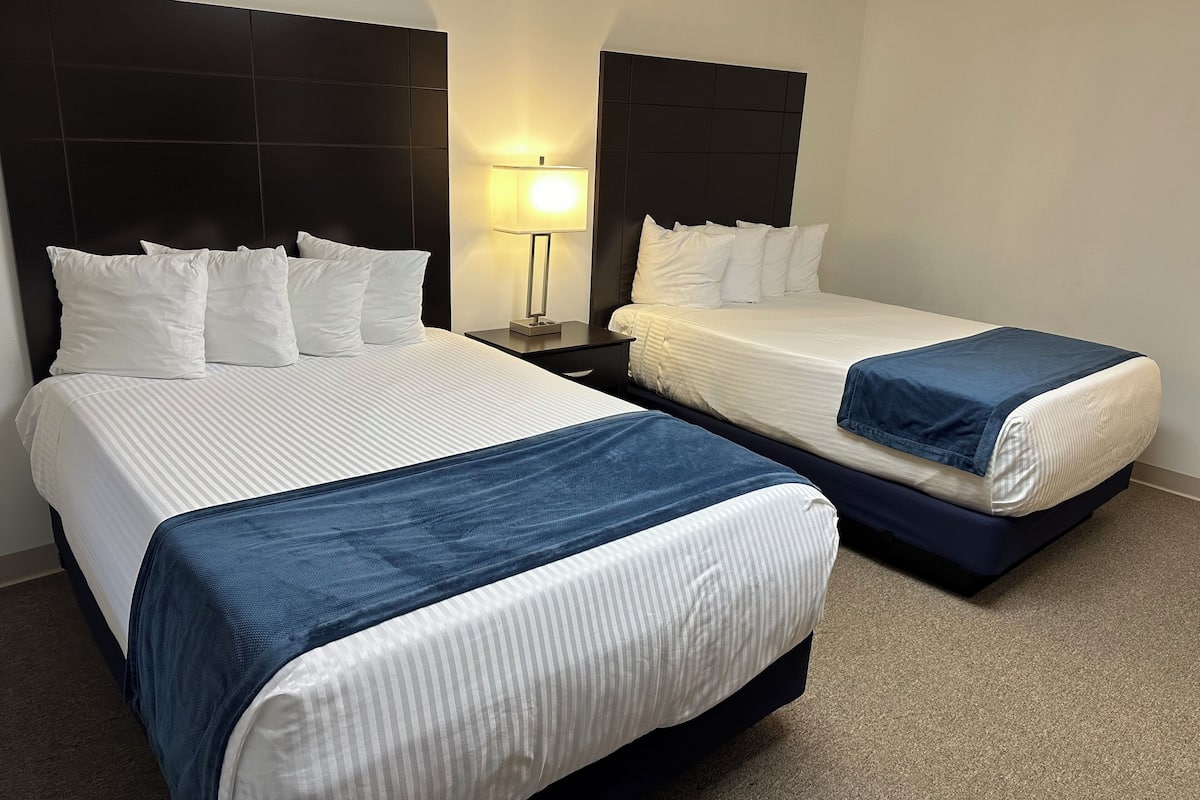 Dos camas con sábanas blancas y cabeceros azules en una habitación de hotel.