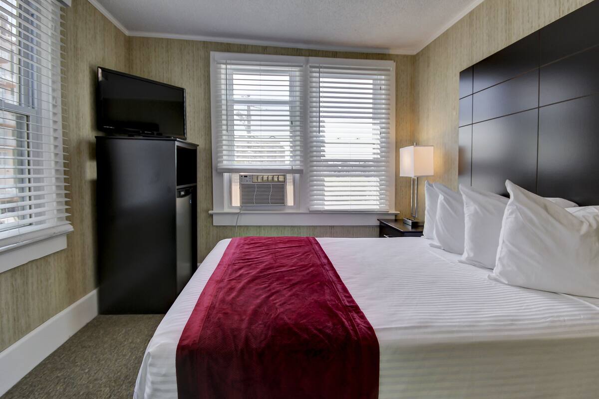 Habitación de hotel con cama, televisor, escritorio y ventana con persianas.