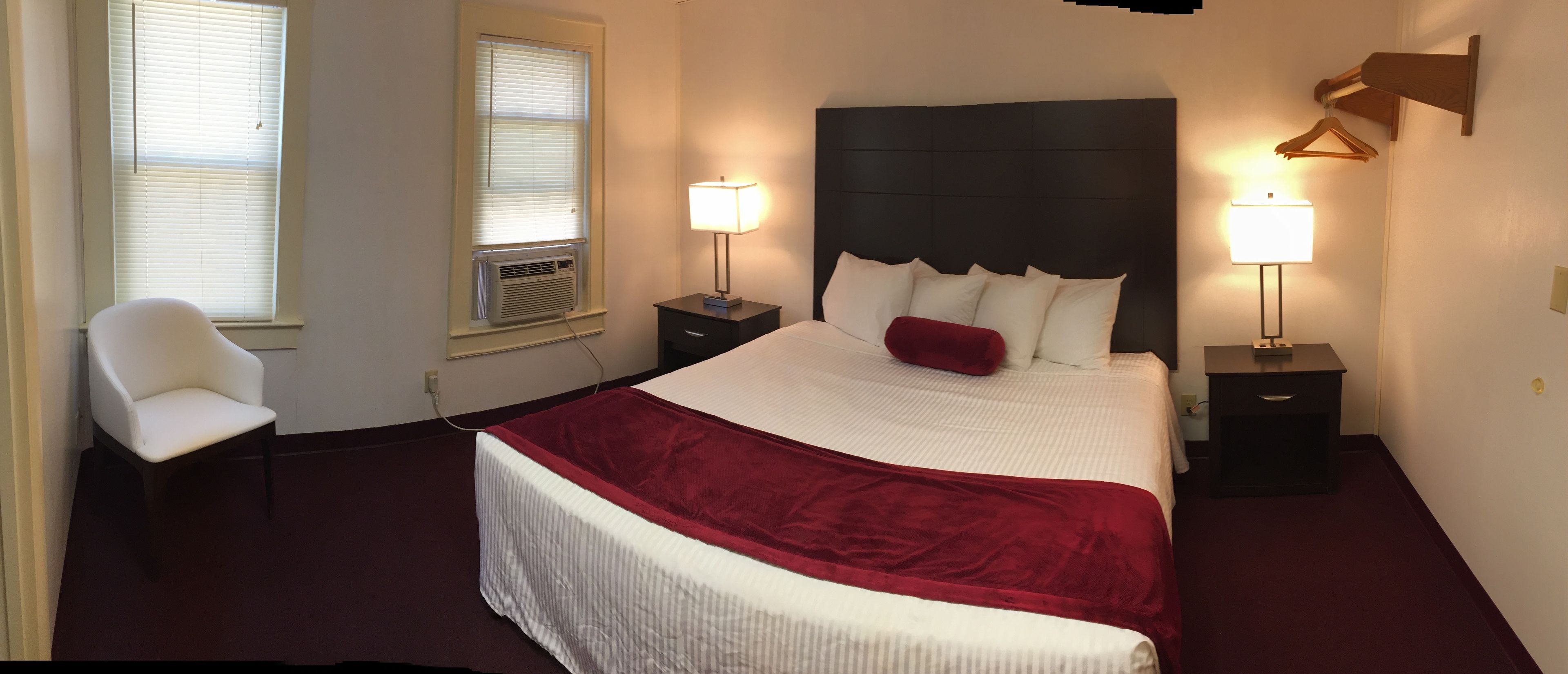 Ein Hotelzimmer mit einem großen Bett, zwei Nachttischen mit Lampen, einem Sessel und einem Fenster mit Jalousien.