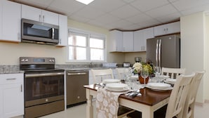 Una cocina moderna con armarios blancos, electrodomésticos de acero inoxidable y una zona de comedor preparada para cuatro personas.