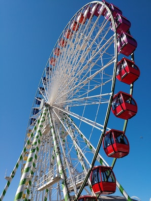 Ein großes Riesenrad mit roten Gondeln vor blauem Himmel.