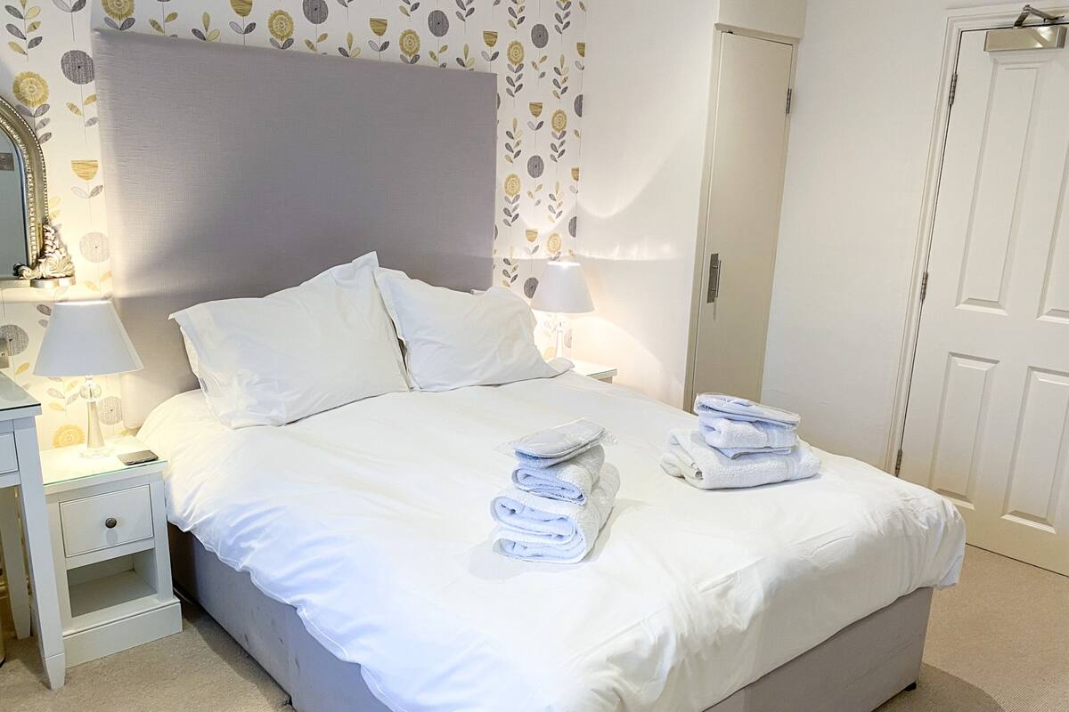 A neatly made bed with white linens and towels, a bedside lamp, and a nightstand with a lamp and a phone.