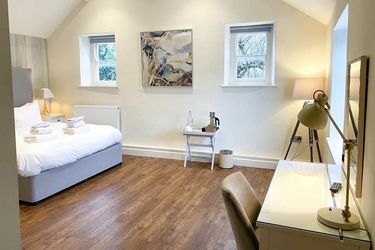 A modern bedroom with a bed, a desk, a chair, a radiator, and two windows.