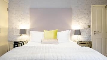 Una cama bien hecha con ropa de cama blanca y una única almohada verde, con dos lámparas de noche a cada lado sobre mesitas a juego.
