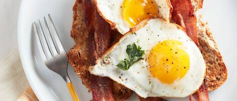 A plate with two fried eggs, bacon, and a fork.