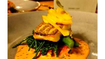 A plated dish with a seared fish, green vegetables, and a creamy sauce.