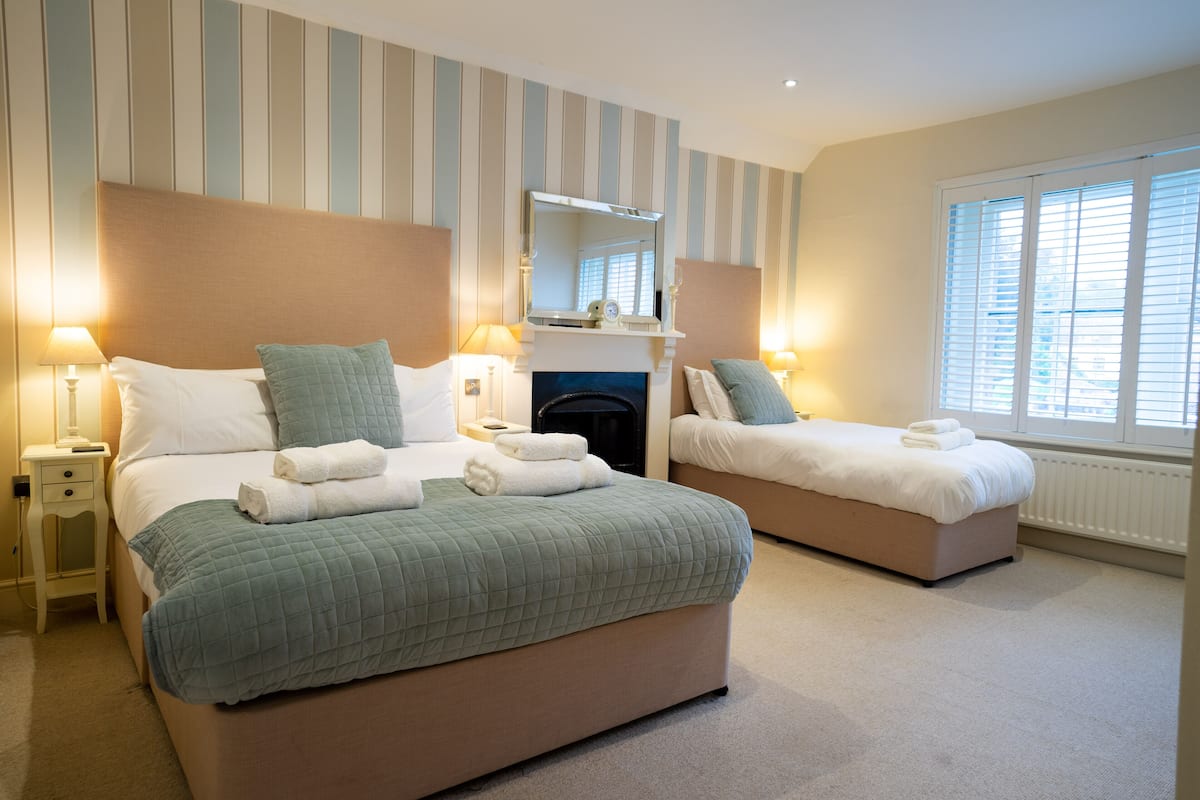 A hotel room with two beds, a fireplace, and a large window with blinds.