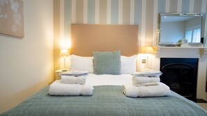 A neatly made bed with a green quilt, two bedside lamps, and a stack of white towels. - The Bear and Swan (Bristol)
