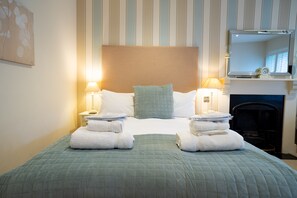 A neatly made bed with a green quilt, two bedside lamps, and a stack of white towels. - The Bear and Swan (Bristol)
