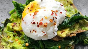 A breakfast dish with a poached egg on toast, avocado, and spinach.