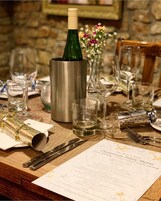 A dining table set for a meal with a menu, wine bottle, glasses, and cutlery.