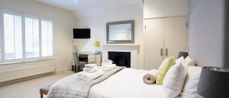 A hotel room with a bed, a desk, a chair, a television, a fireplace, and a window with blinds.