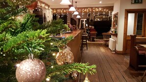 A cozy bar area with wooden flooring, a Christmas tree, and hanging string lights. - The Bear and Swan (Bristol)