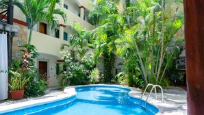 A swimming pool surrounded by lush greenery and a building with multiple balconies. - Magic Paradise by Bric (Playa del Carmen)
