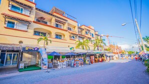 A street with outdoor seating, palm trees, and a building with balconies. - Magic Paradise by Bric (Playa del Carmen)