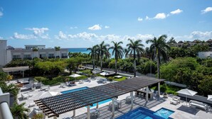 Zwembad van een resort met helder uitzicht op de oceaan, omringd door palmbomen en ligbedden.