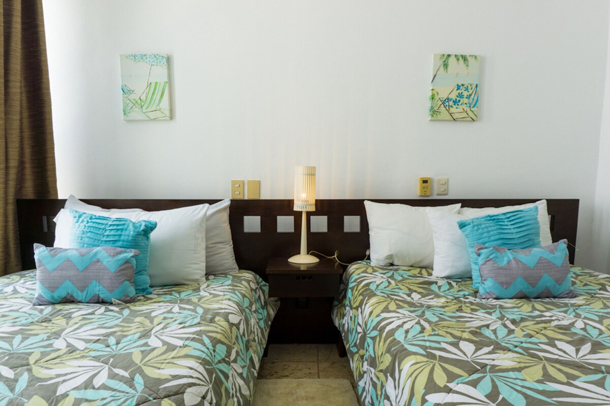 Une chambre d’hôtel avec deux lits, une table de chevet avec une lampe et des œuvres d’art accrochées aux murs.
