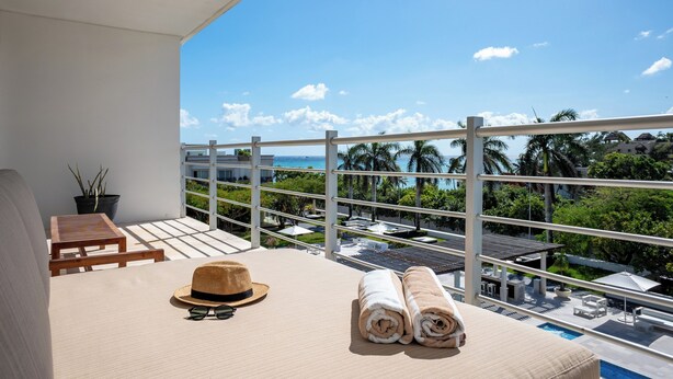 Een balkon met uitzicht op de oceaan, een hoed, zonnebril en handdoeken op een bed.