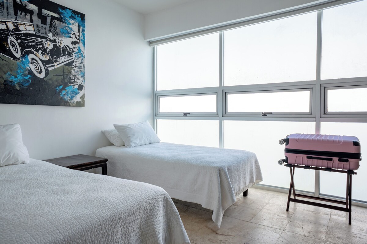 Une chambre d’hôtel avec deux lits, une grande fenêtre et un tableau au mur.