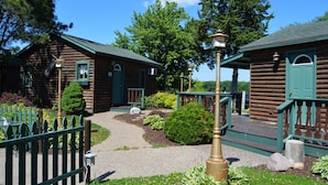 A rustic log cabin with a gravel pathway leading to the entrance, surrounded by greenery and a wooden fence. - Moon River Cabins (Bellevue)