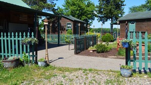 A rustic log cabin with a green picket fence, surrounded by potted plants and a gravel path. - Moon River Cabins (Bellevue)