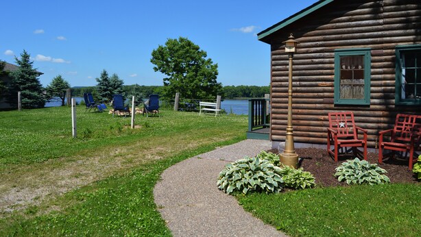 A log cabin with a gravel path leading to a dock, surrounded by greenery and a lake view. - Moon River Cabins (Bellevue)