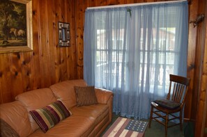 A wooden interior with a leather sofa, a wooden chair, and a window with sheer curtains. - Moon River Cabins (Bellevue)