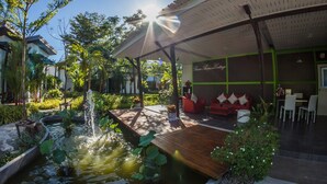 A modern outdoor area with a wooden deck, a small pond with lily pads, and a red sofa under a pergola. - Baan Armeen Cottage (Choeng Thale)