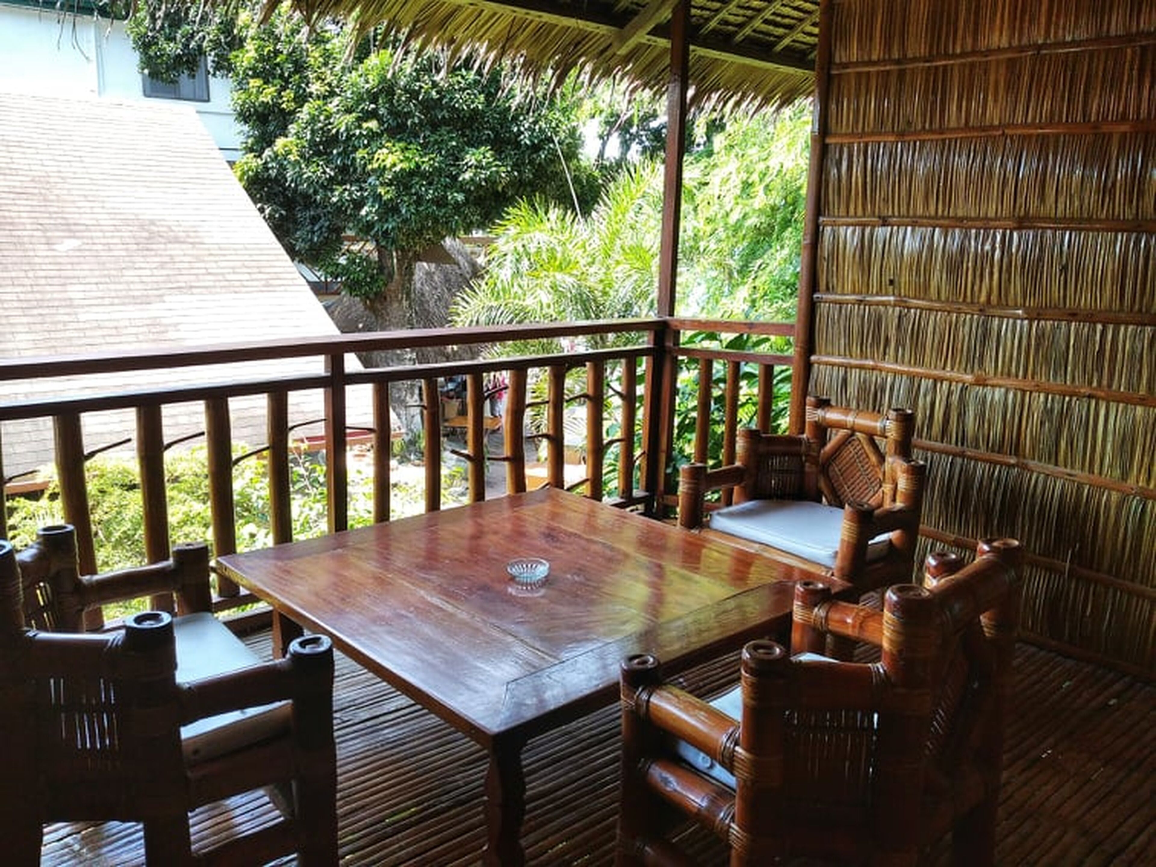 Una terraza de madera al aire libre con una mesa y sillas, rodeada de exuberante follaje.