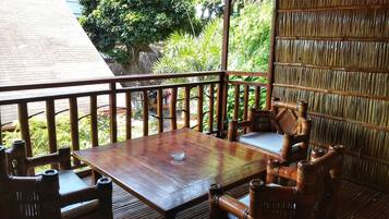 Una terraza de madera al aire libre con una mesa y sillas, rodeada de exuberante follaje.