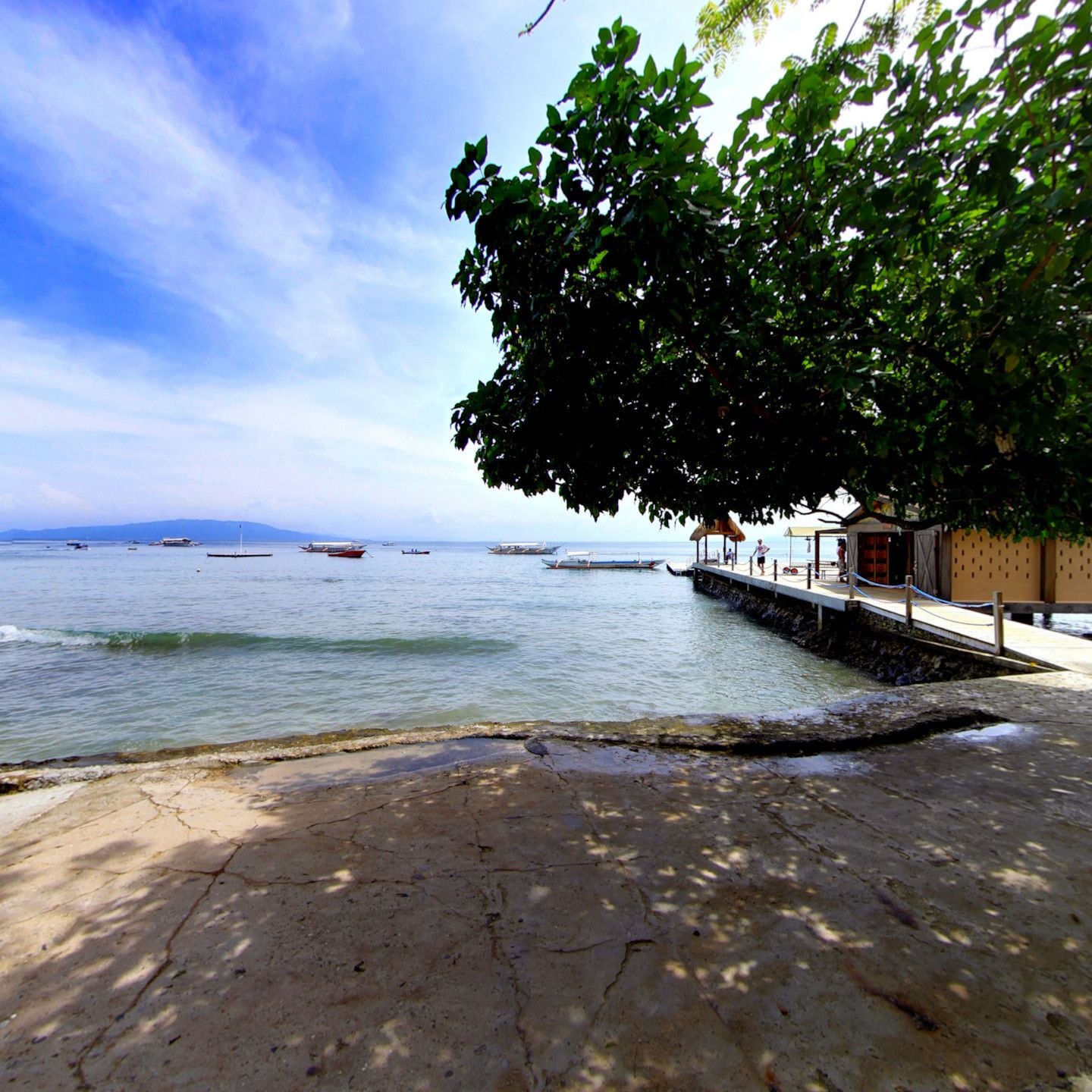 A beach with boats, a pier, and a building with a tiled roof.