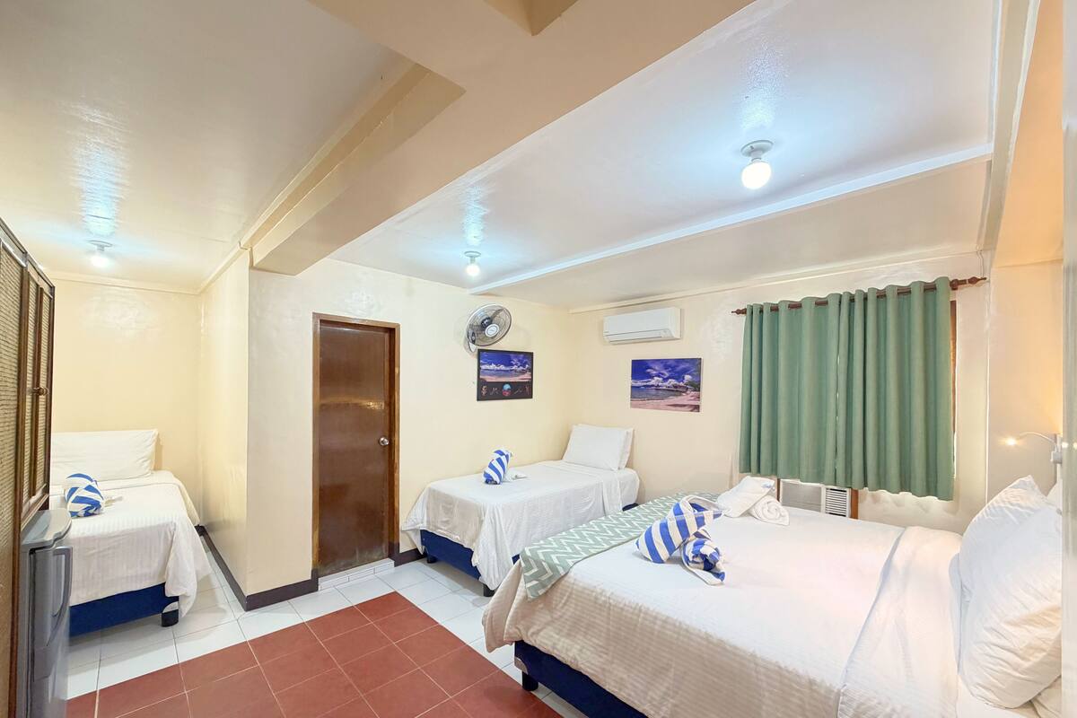 A hotel room with two beds, a fan, an air conditioner, and a view of the beach.