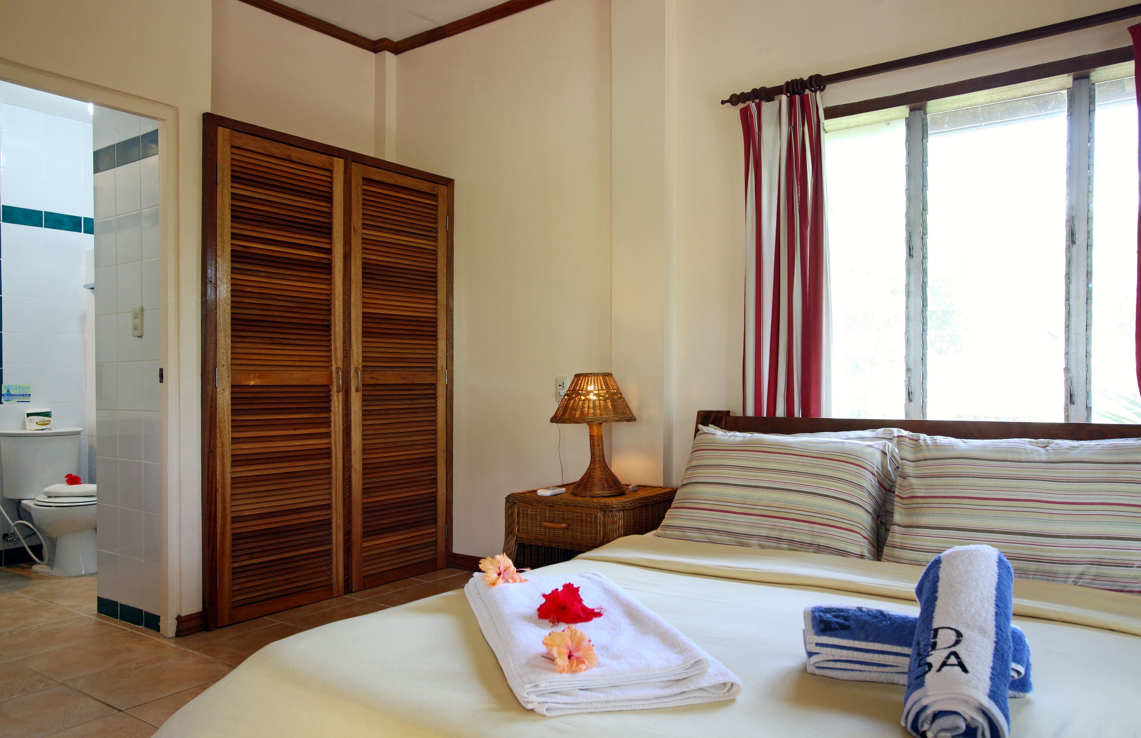 A hotel room with a bed, a nightstand with a lamp, a wardrobe, and a window with curtains.