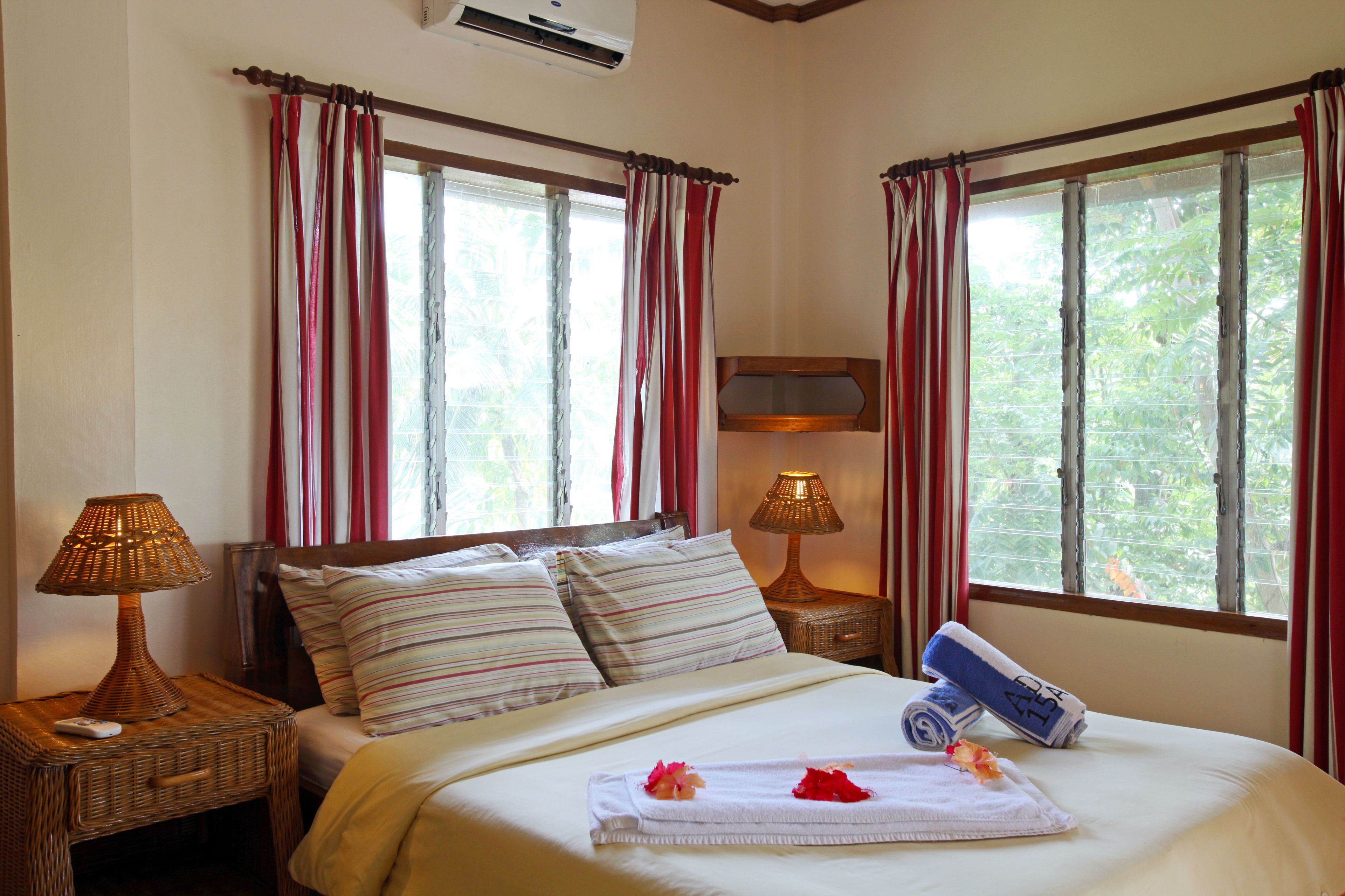 A neatly made bed with striped pillows, a bedside lamp, and a rolled towel on the bed.