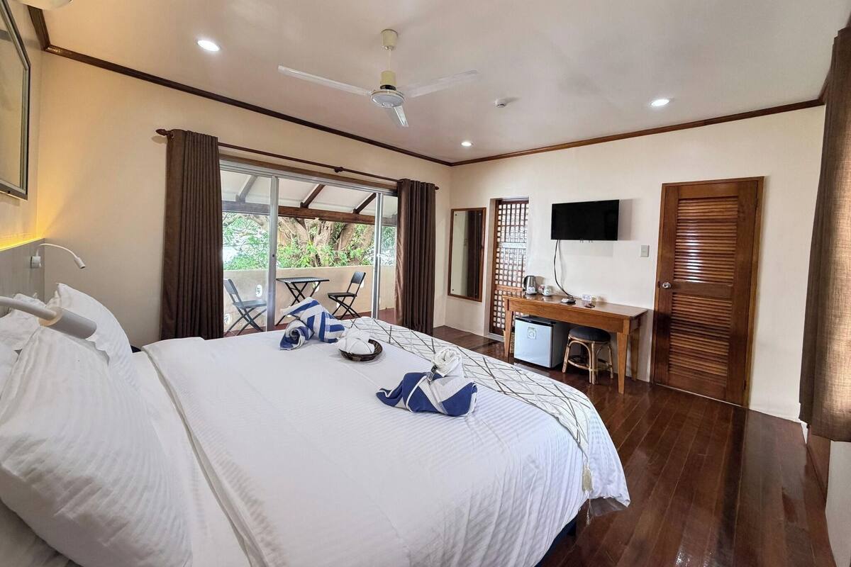 A hotel room with a bed, a desk, a television, and a balcony with a view.