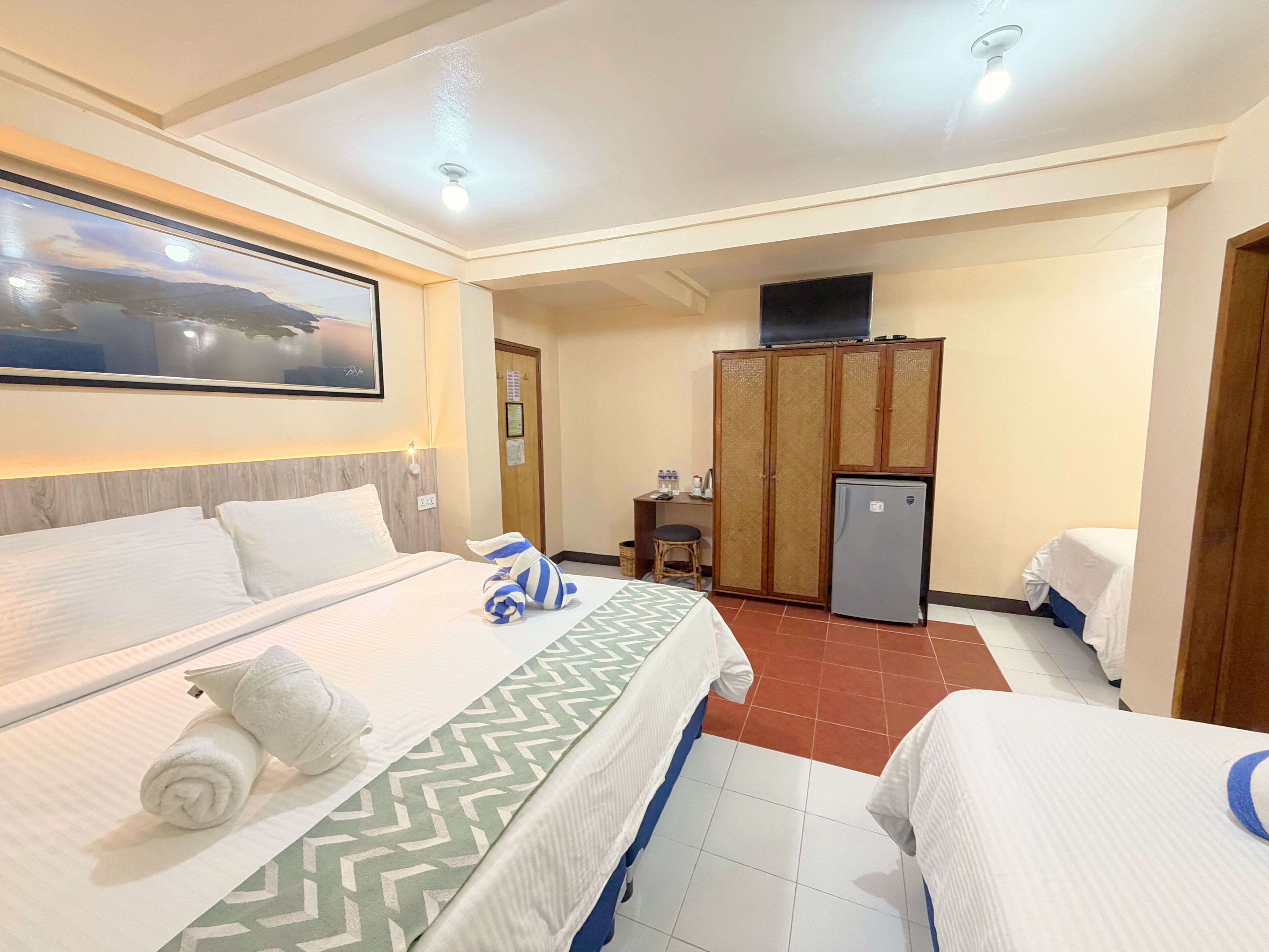 A hotel room with two beds, a desk with a chair, a refrigerator, and a large window with a view.