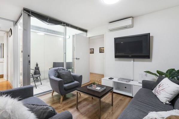 A modern living room with a grey sofa, a coffee table, and a flat-screen TV mounted on the wall. - Anchor on Collins (Melbourne)