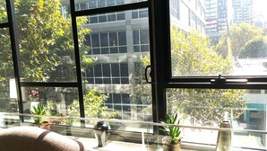 A room with large windows, a sofa, and several potted plants on a windowsill. - Anchor on Little Collins - Southern (Melbourne)