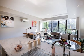 A modern kitchen with a glass island, a sink, and a dining area with a sofa and chairs. - Anchor on Little Collins - Southern (Melbourne)